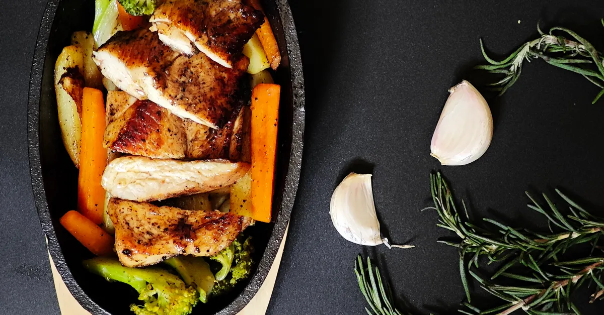 Sliced chicken sizzling in a cast iron skillet with carrots and broccoli