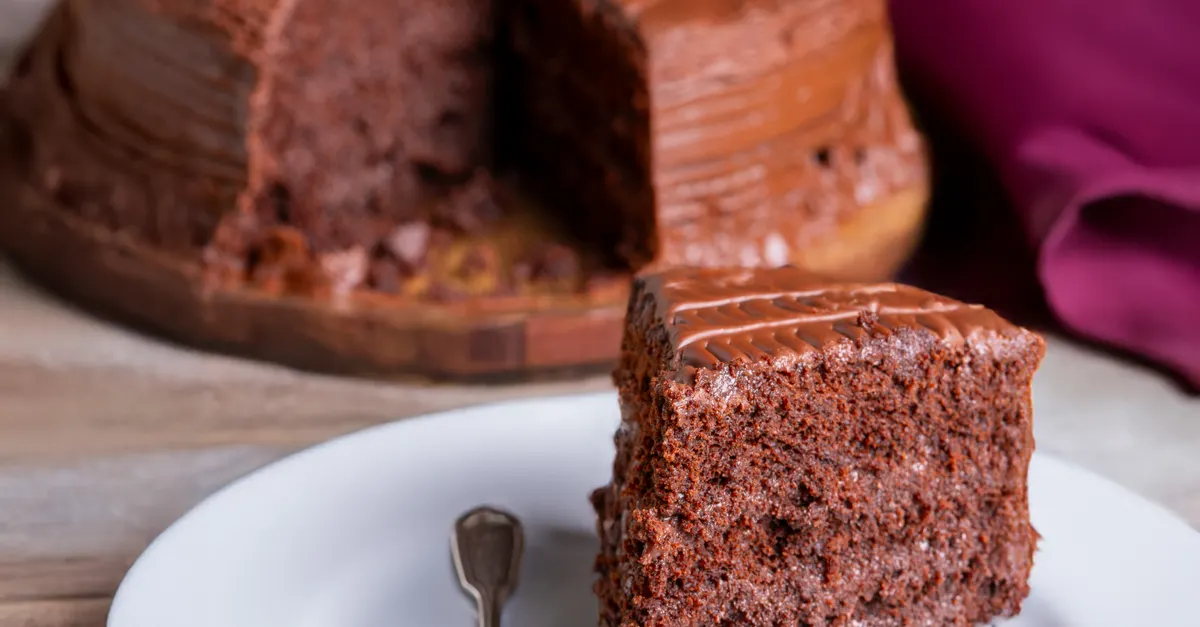 Rich dark chocolate cake with a slice cut, showing moist chocolate layers on a white plate
